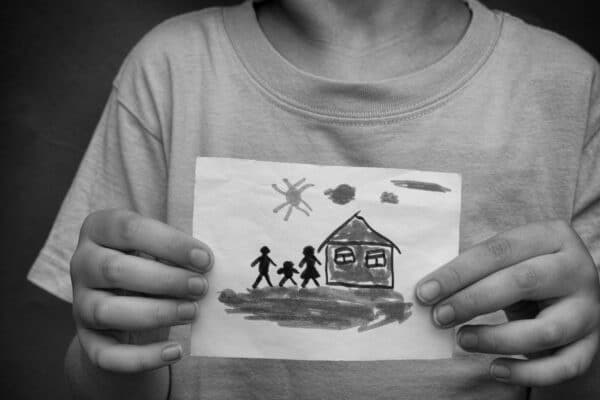 Child holds a drawn house with family. Close up.