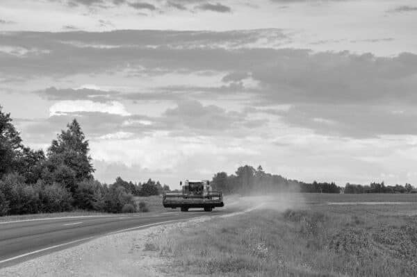 Combine harvester traveling on a rural highway beside farm fields during harvest season